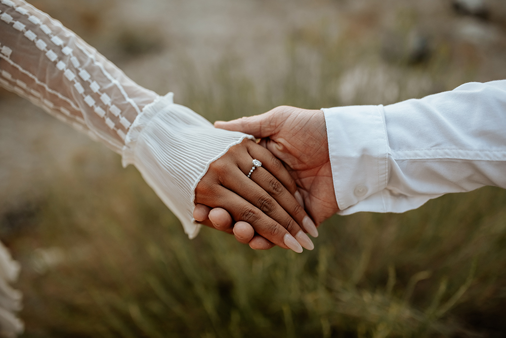 Hands close-up of boho couple in nature holding hands and walking, hugging having fun for their engagement photo session.