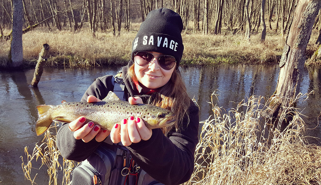 a happy smiling woman holding a trout that she has caught fishing