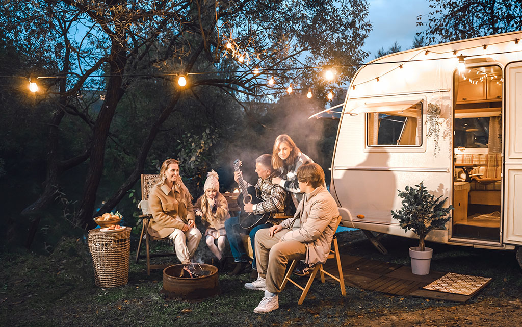 Family trailer travel.Children,brother sister,mom dad playing guitar,singing song at fire.Evening picnic in nature.Holiday barbecue BBQ food.Vacation weekend dinner.Road lunch.Camper,house on wheels.