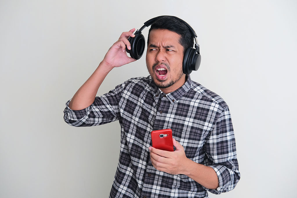 Adult Asian man showing can not hear to someone gesture when listening music