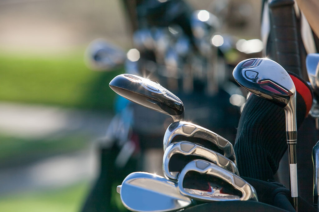 Golf clubs glistening in the sunlight. A golf bag full of clubs. Golf club heads.