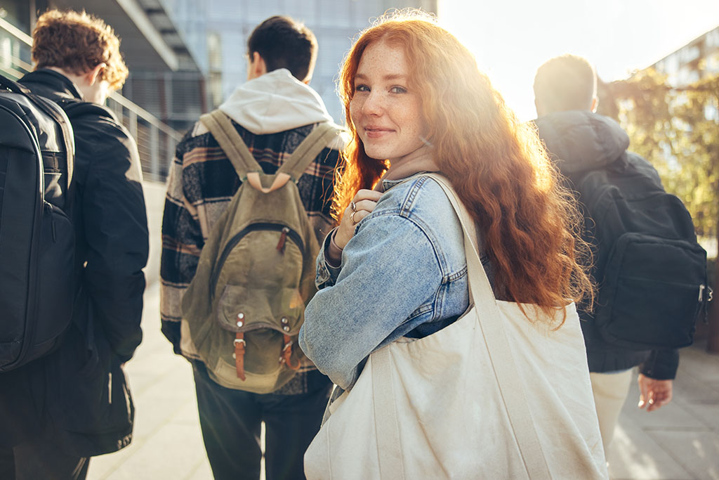 Female student glancing back while going for a class in college. Girl walking with friends going for class in high school.