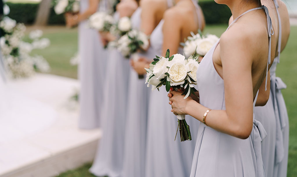 Bridesmaids in dresses stand with bouquets of flowers in a row