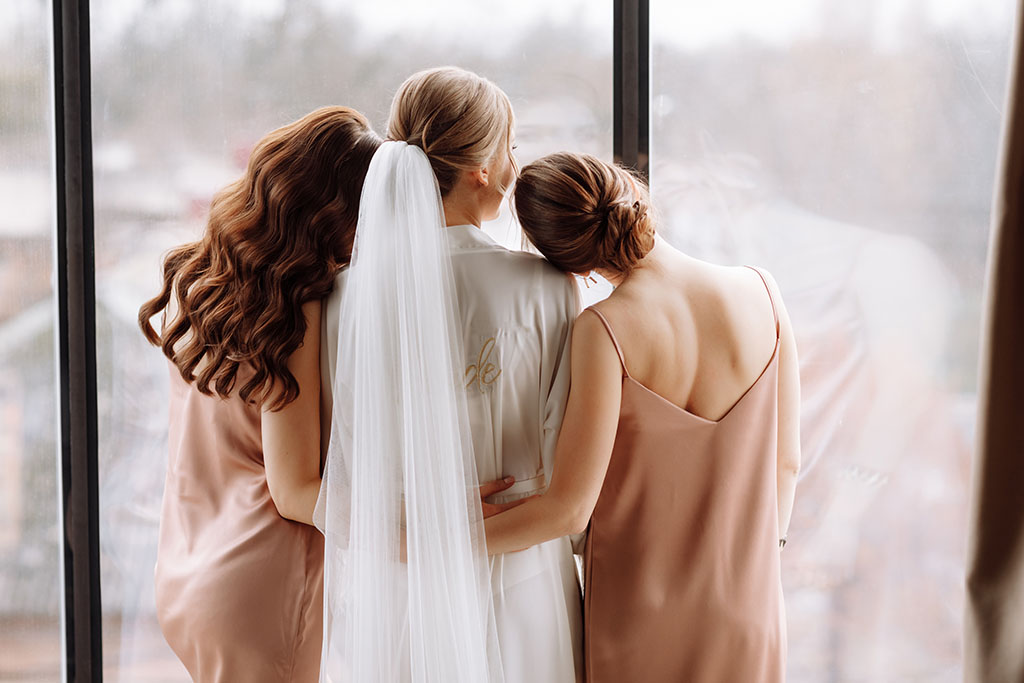 Morning of bride. Gorgeous bride with best bridesmaids are having fun in hotel room near the large window. Sexy bridesmaids in exciting negligee. Wedding morning details. back view.