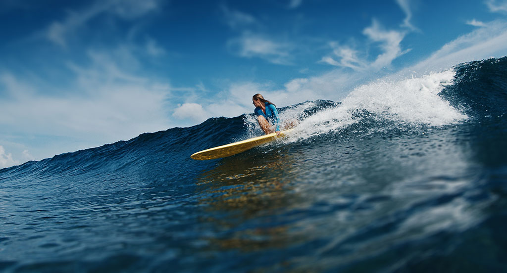 Slim woman surfer rides the wave. Woman surfs the ocean wave in the Maldives on yellow longboard