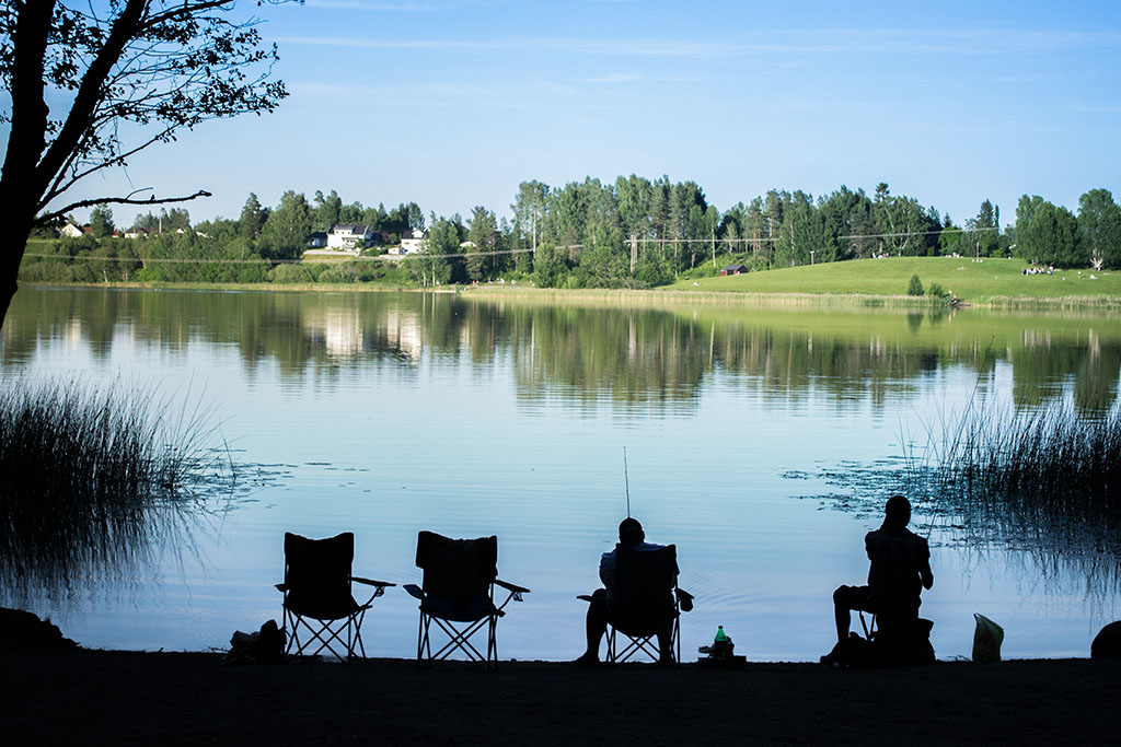 A group of fishermen fishing on a lake. The fishermen and the whole foreground are blacked-out to give a more romantic silhouette  look.. A mirror image of the other shore can be seen on the lake.